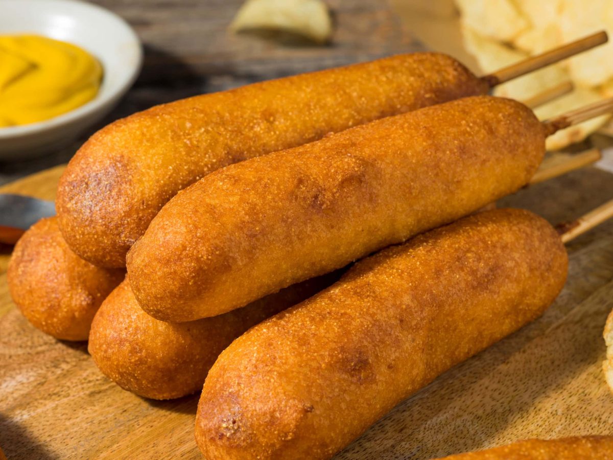 seitliche aufnahme von corn dogs mit senfschale im hintergrund auf holzbrett