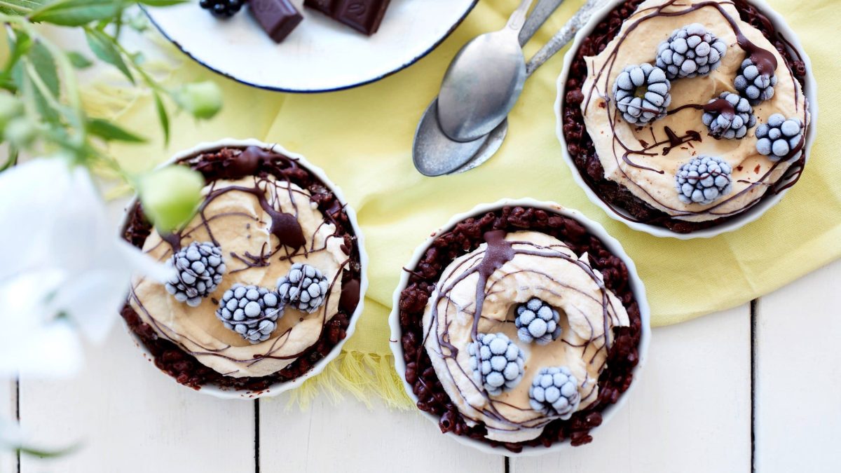 in Schüssel sind Eis-ähnliche Crispy Erdnuss-Törtchen angerichtet. Sie sind mit Schokosauce überzogen und mit Brombeeren dekoriert.