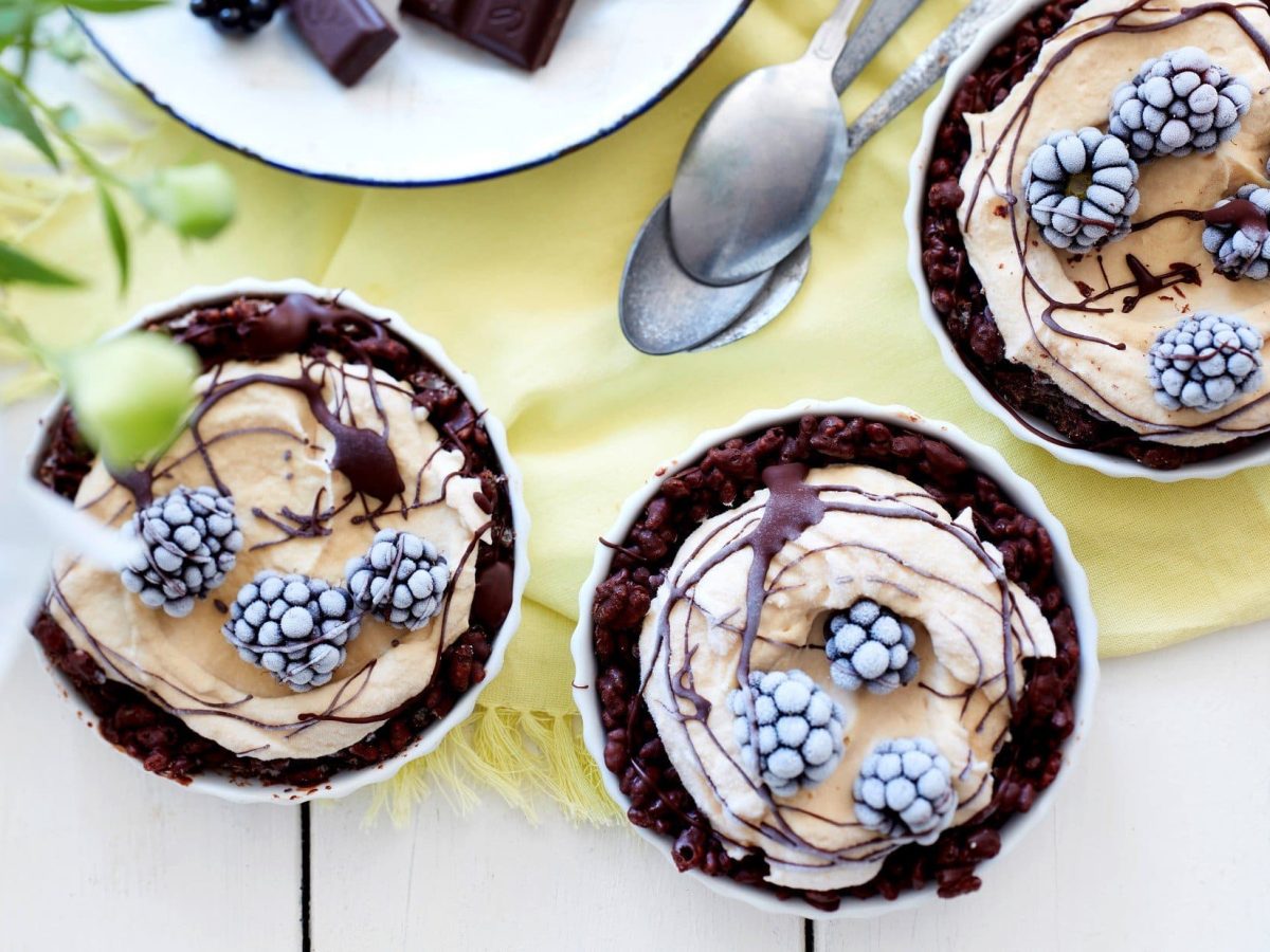 in Schüssel sind Eis-ähnliche Crispy Erdnuss-Törtchen angerichtet. Sie sind mit Schokosauce überzogen und mit Brombeeren dekoriert.