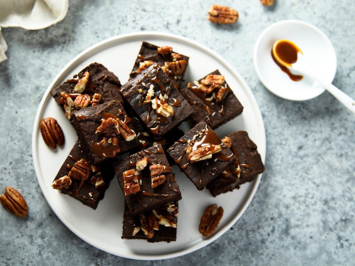 Auf einem weißen Teller liegen mehrere Stück Brownies mit Pekannüssen. Sie sind mit einem Klecks Schokoladensoße und Pekannüssen verziert.