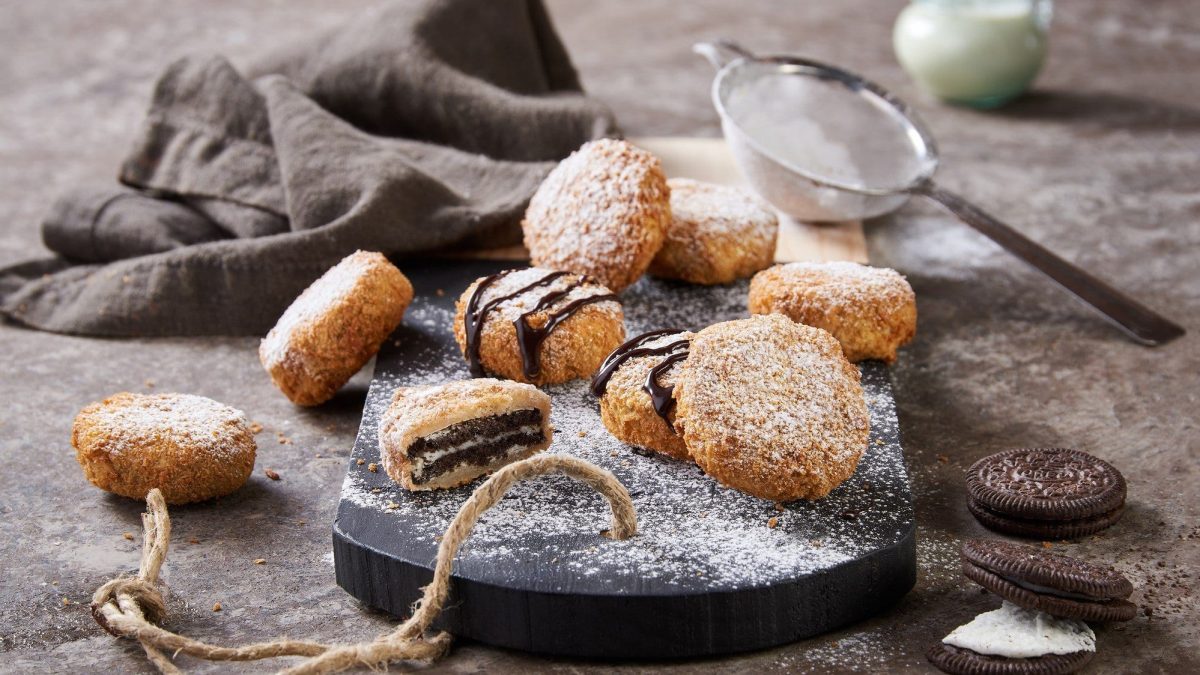 Auf einer Holzplatte liegen einige fritterite Oreos. Sie sind mit Schokosauce und Puderzucker dekoriert.