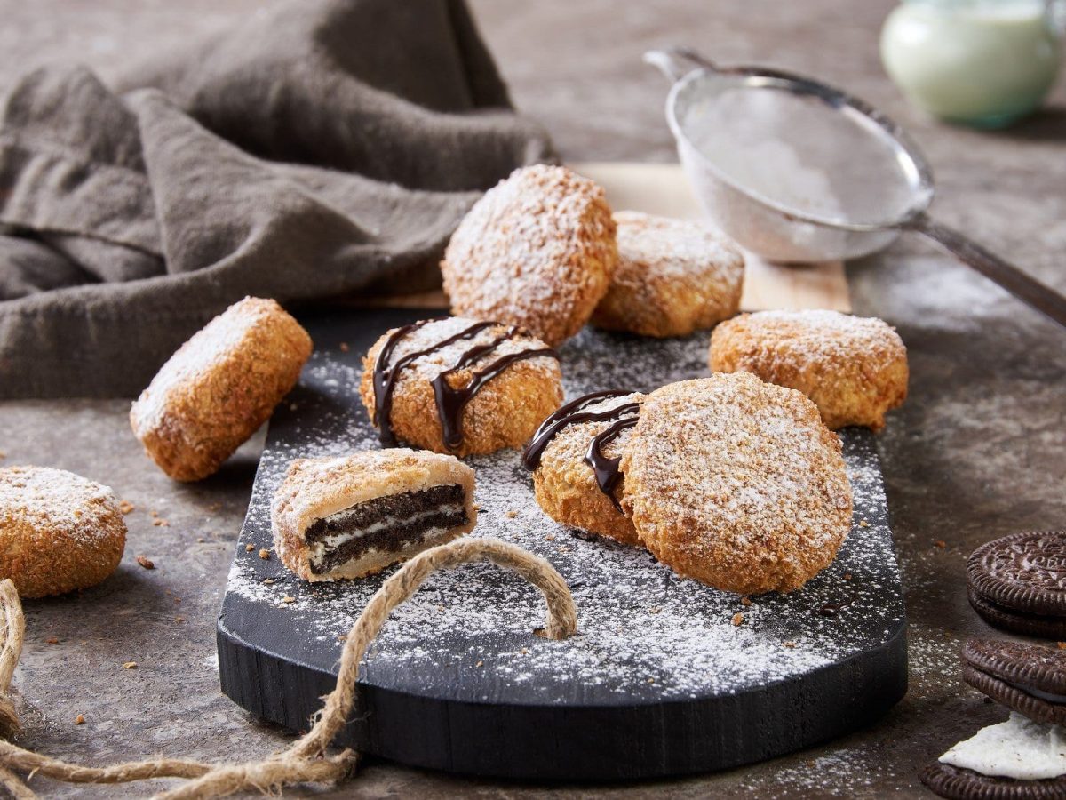 Auf einer Holzplatte liegen einige fritterite Oreos. Sie sind mit Schokosauce und Puderzucker dekoriert.