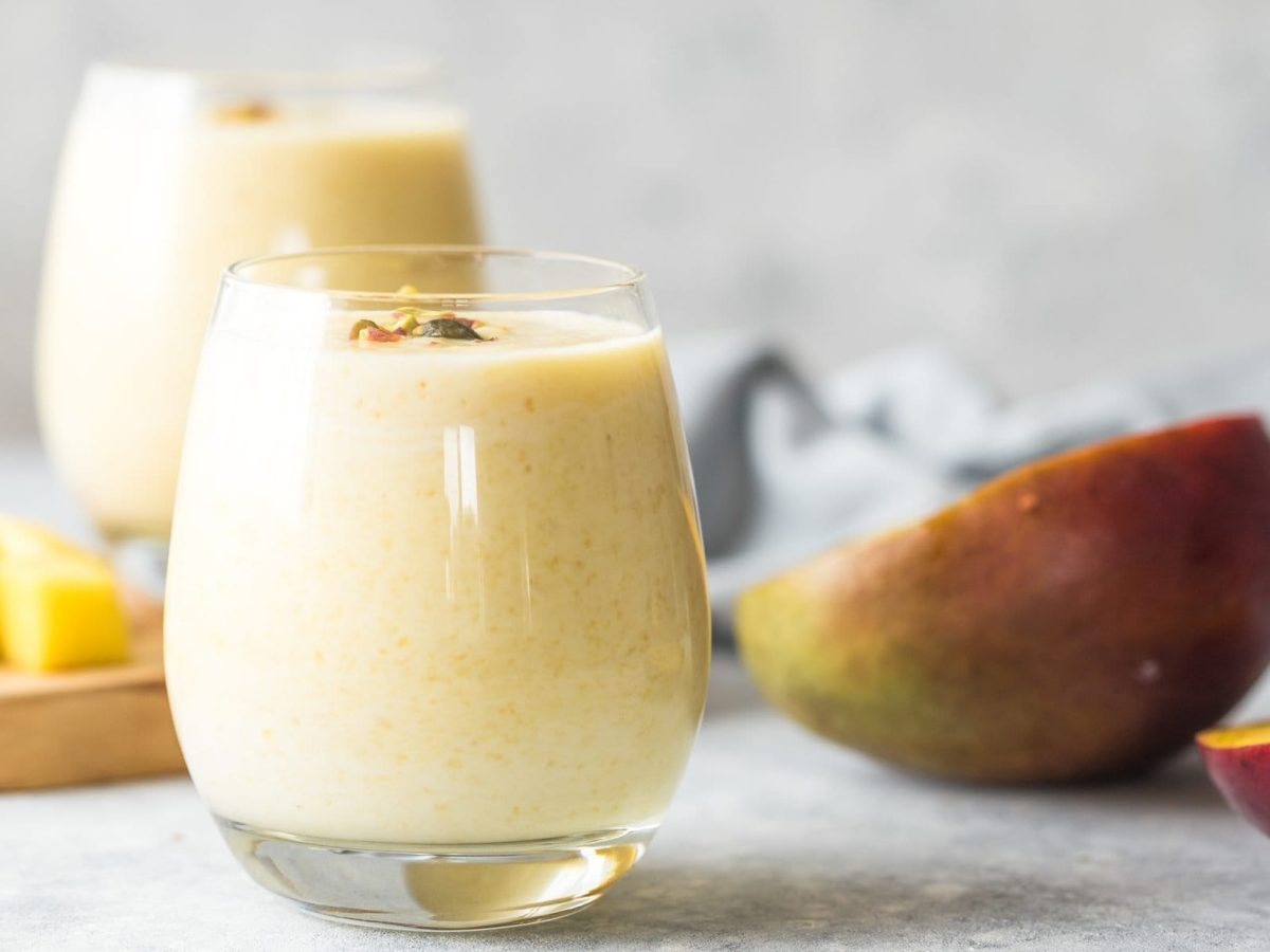 Ein Glas Kefir-Smoothie im Vordergrund, eines im Hintergrund. Mango zusätzlich als Deko.