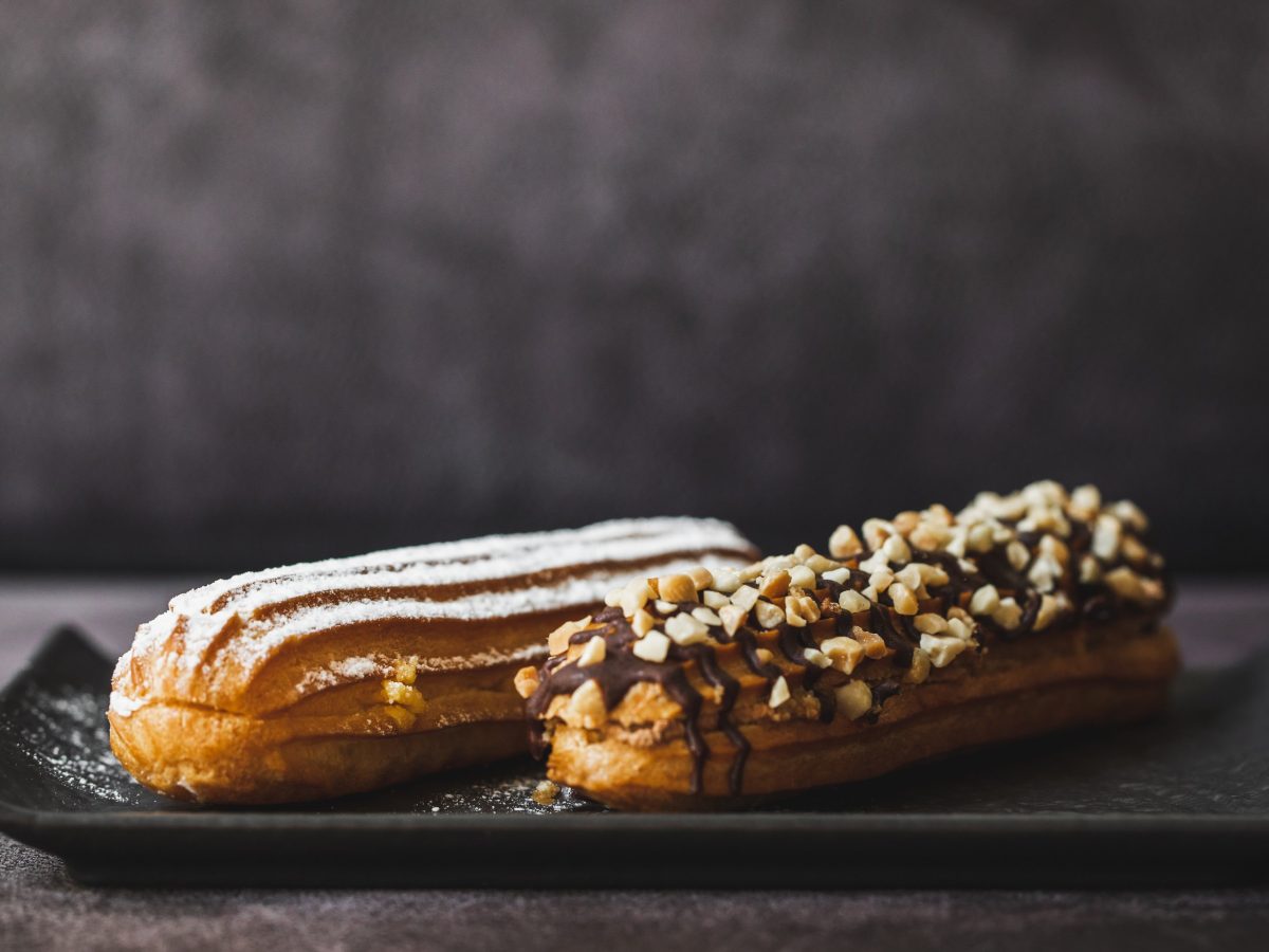 Zwei Eclairs von der Seite auf schwarzem Teller.