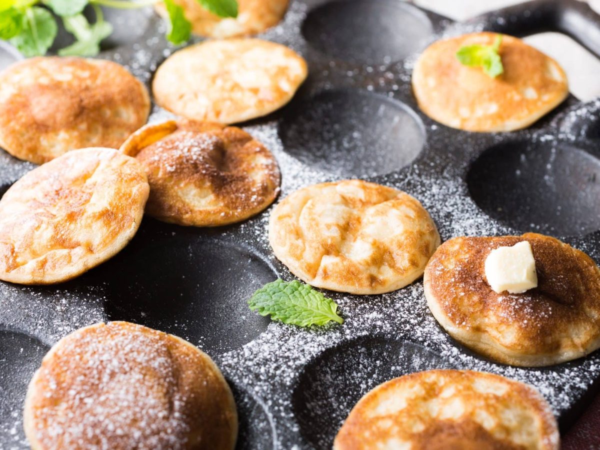 Die kleinen Poffertjes liegen mit Puderzucker bestäubt direkt in der speziellen Pfanne, in der sie gebacken wurden.