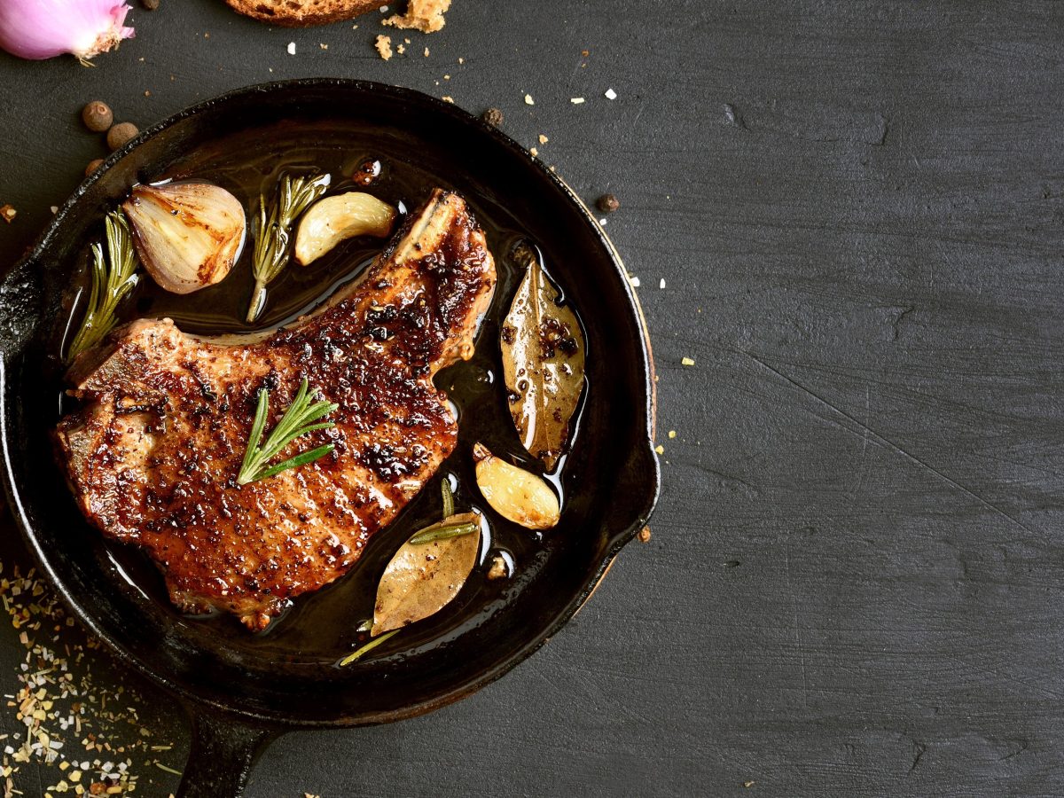 pfanne mit fleisch und gewürzen von oben auf schwarzem tisch