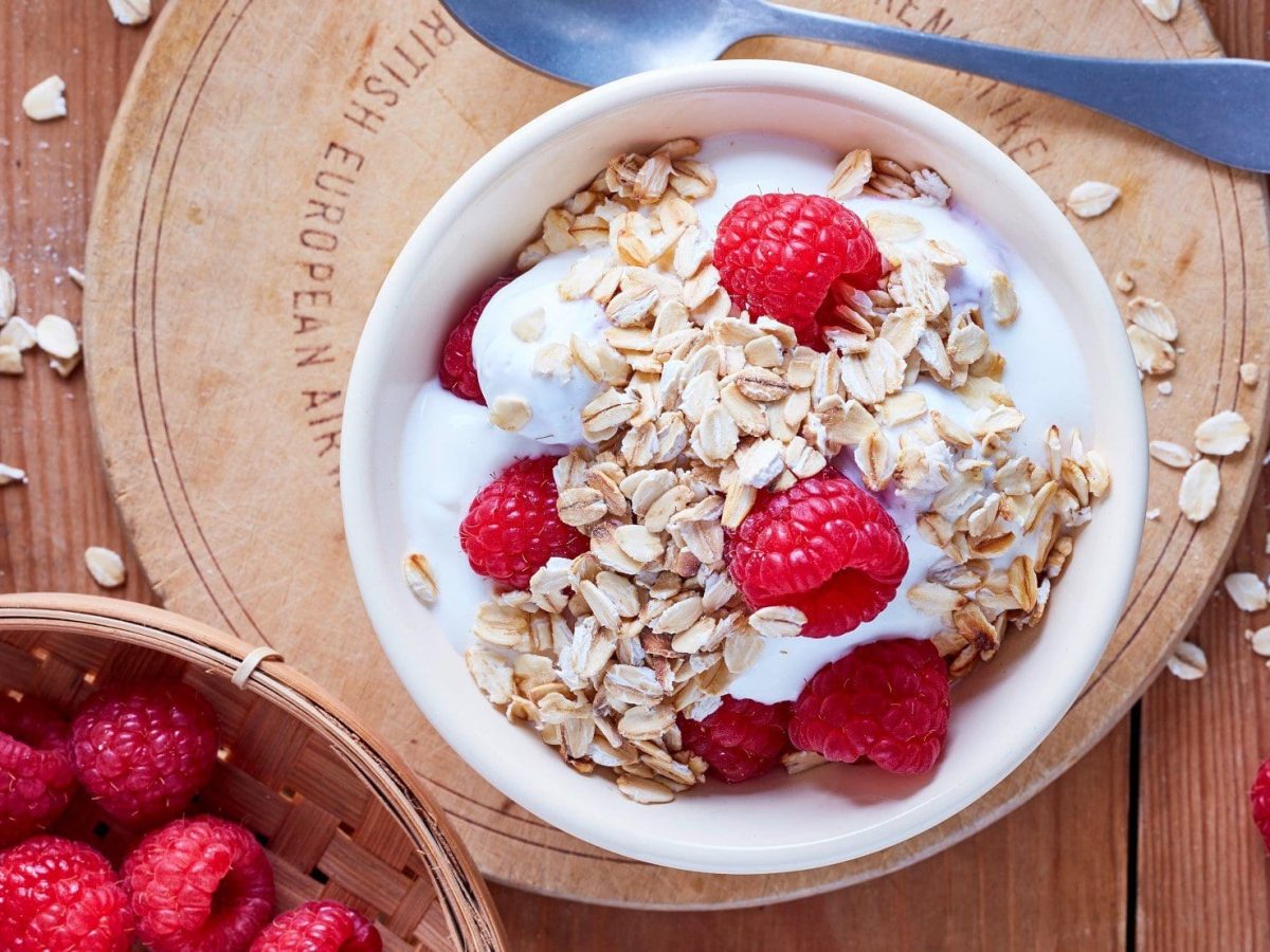 In einer Schüssel ist ein Haferflocken-Frucht-Quark angerichtet. Oben drauf sind frische Himbeeren.