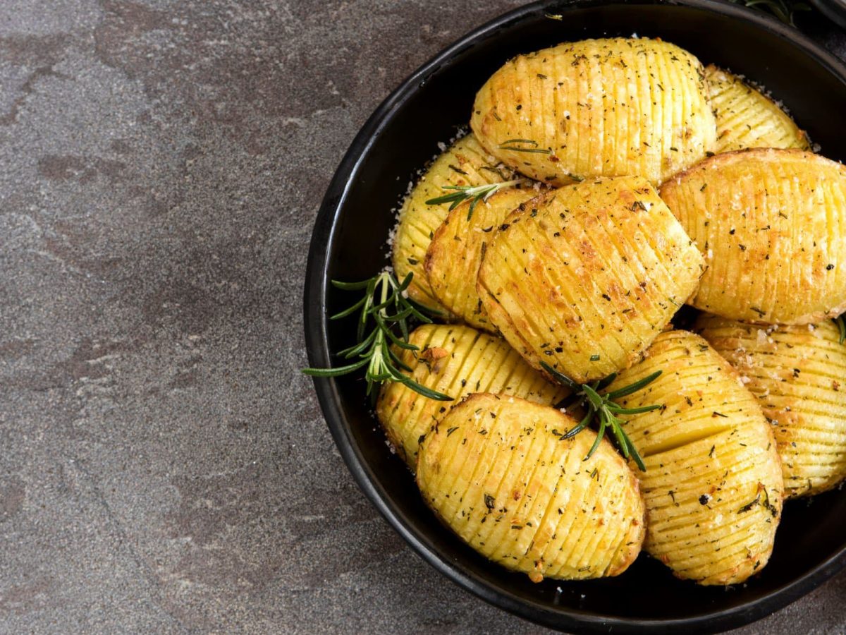 Hasselback-Kartoffeln mit Rosmarin auf schwarzem Teller.