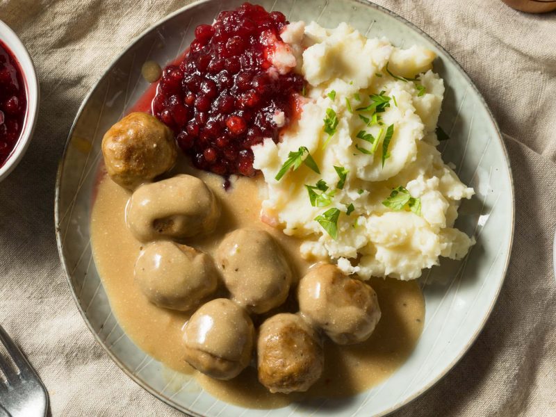 Köttbullar mit Soße, Preiselbeeren und Kartoffelpüree auf hellem Tischtuch.