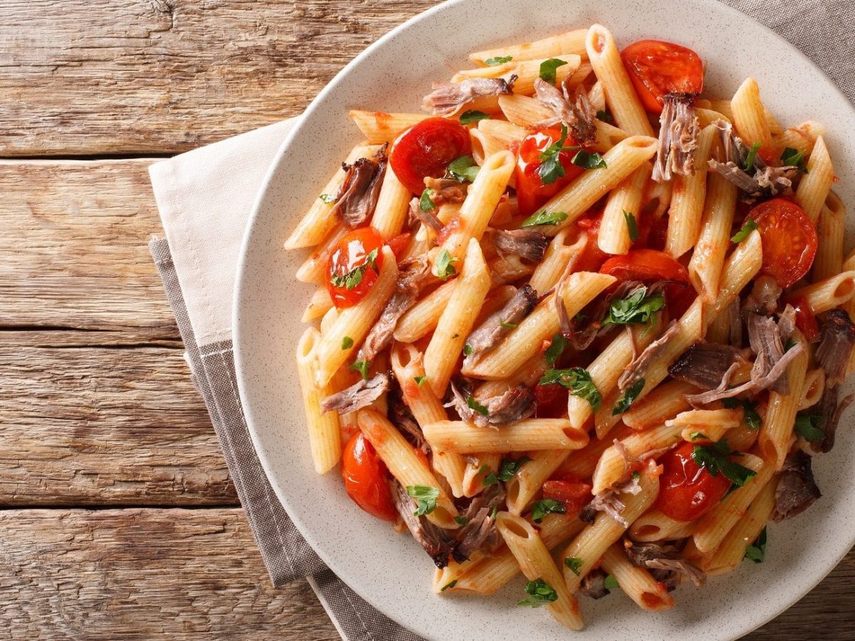 Ein prallgefüllter Teller mit unserer Pulled-Pork-Pasta steht auf einem Holztisch.