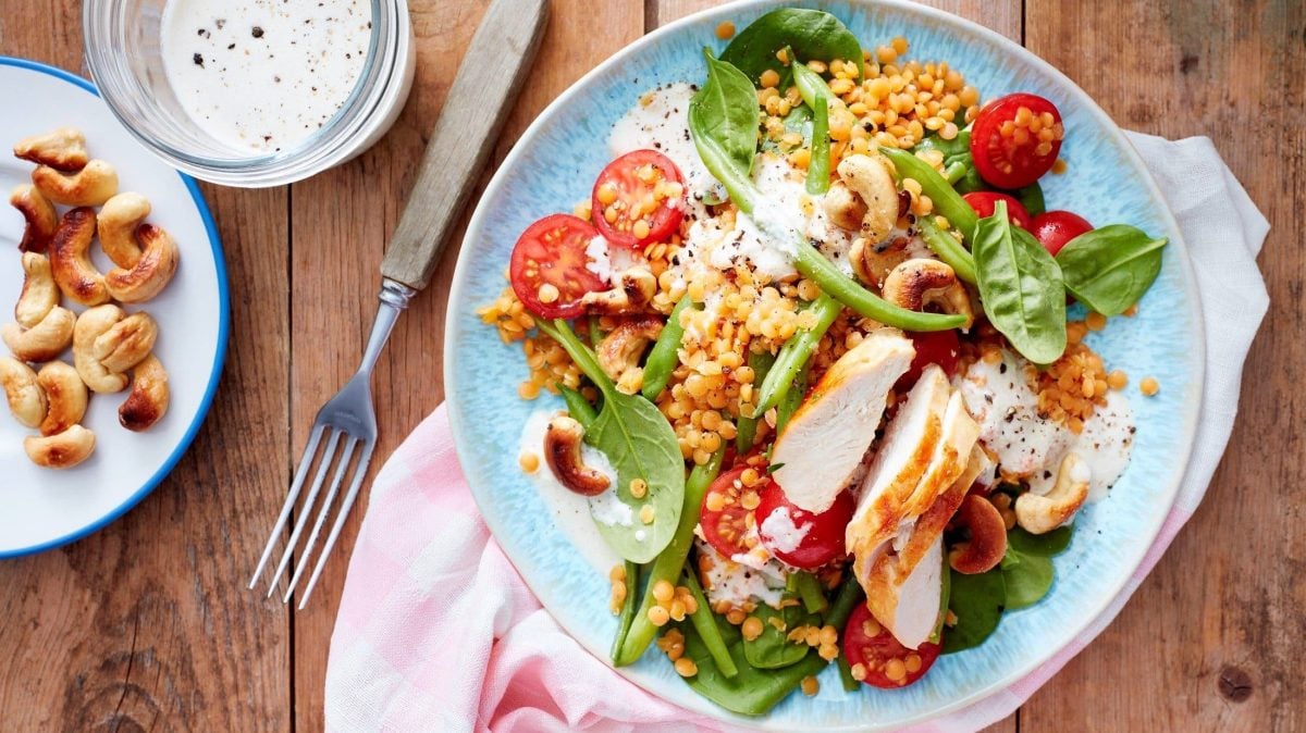 Unser roter Linsensalat mit Cashewdressing und vielen weiteren aromatischen Zutaten angerichtet auf einem Teller. Cashewnüsse liegen auf einem Teller daneben.