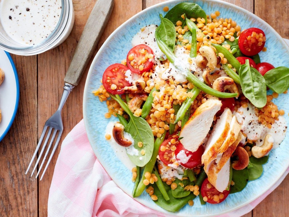 Unser roter Linsensalat mit Cashewdressing und vielen weiteren aromatischen Zutaten angerichtet auf einem Teller. Cashewnüsse liegen auf einem Teller daneben.