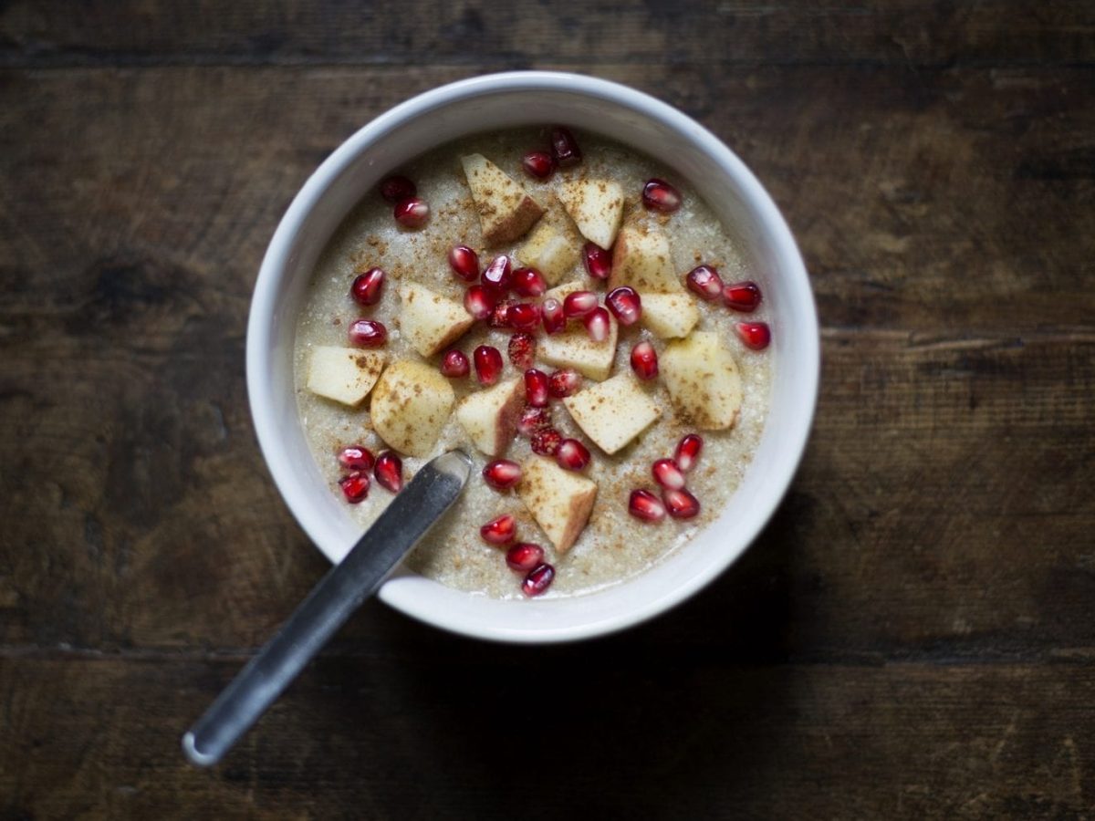 Aus der Vogelperspektive: Auf einem dunklen Holztische steht eine Schüssel mit Apfel-Zimt-Porridge. In der Schüssel ist ein Löffel.