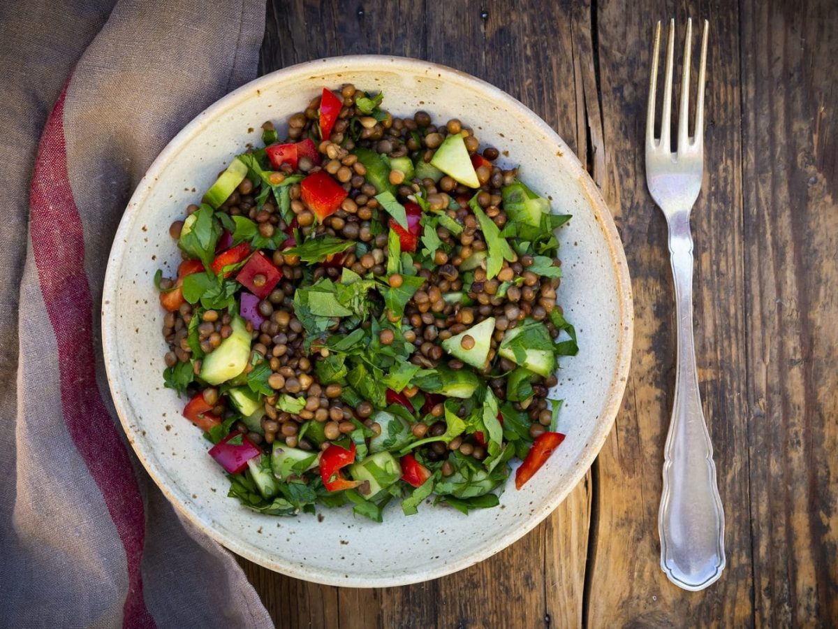 Aus der Vogelperspekttive: Auf einem Tisch steht ein teller mit einem warmen Balsamico-Linsen-Salat. Daneben liegt eine Gabel.