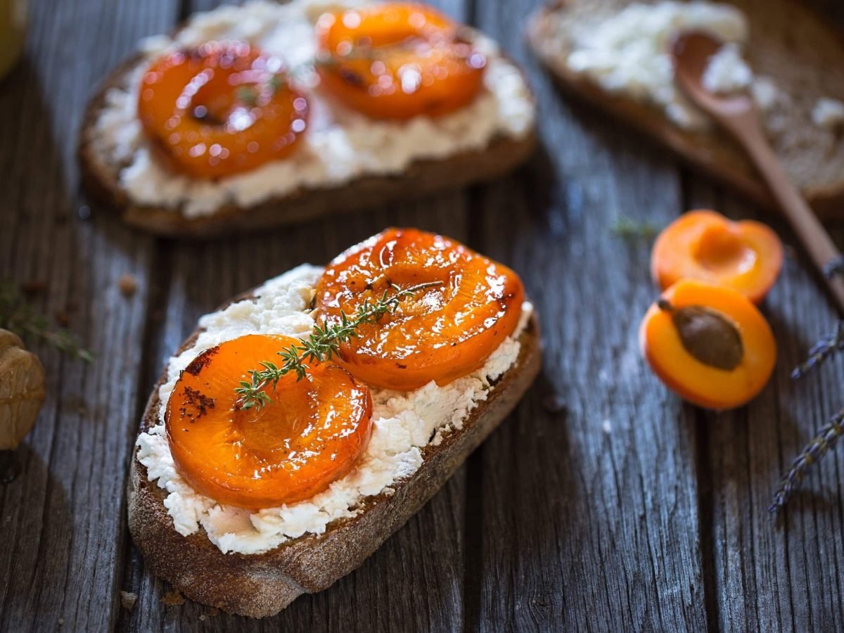 Knursprige Crostinis mit Ziegenkäse und Aprikose, garniert mit Thymian und Honig auf einer Holzplatte mit frischen Lavendelblättern im Hintergrund