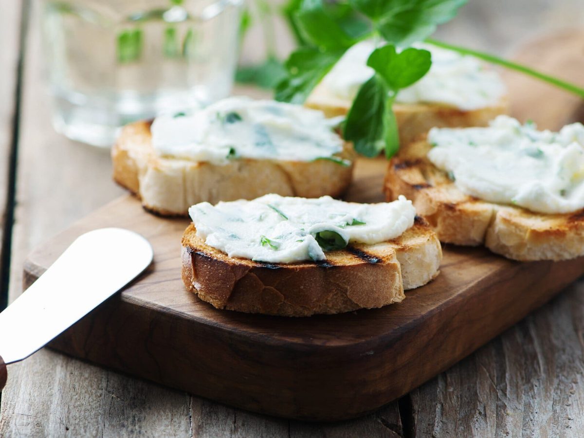 Getoastete Brotscheiben mit selbst gemachtem Frischkäse auf einem Brett, daneben liegt ein Messer.