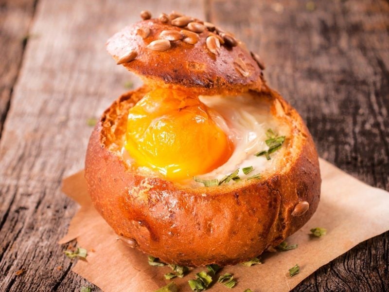 Unsere Frühstücks-Bowl im Brötchen steht auf Backpapier auf einem Holztisch.