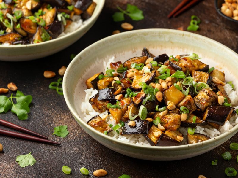 Gebratene Aubergine mit Erdnusssauce und Reis, Frühlingszwiebeln und Erdnüssen.