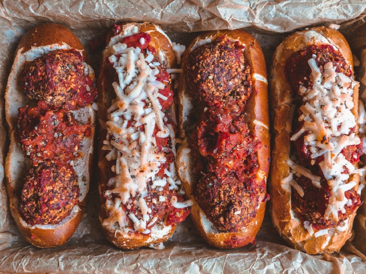 Gefüllte Laugenstangen mit Hackbällchen, Tomaten und Käse liegenin einer mit Backpapier ausgelegten Backform.