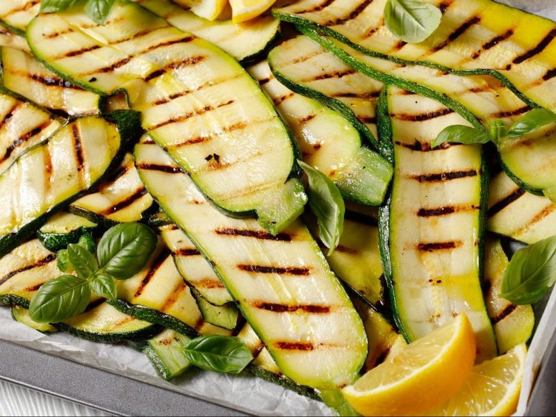 Aus der Vogelperspektive: Auf einem Blech liegen gegrillte Zucchini mit Basilikum und Zitronenscheiben.