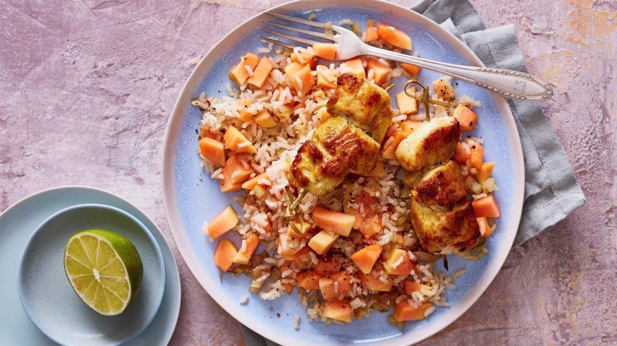 Unsere krossen Hähnchen-Spieße liegen auf fruchtigem Papaya-Salat auf einem Teller.