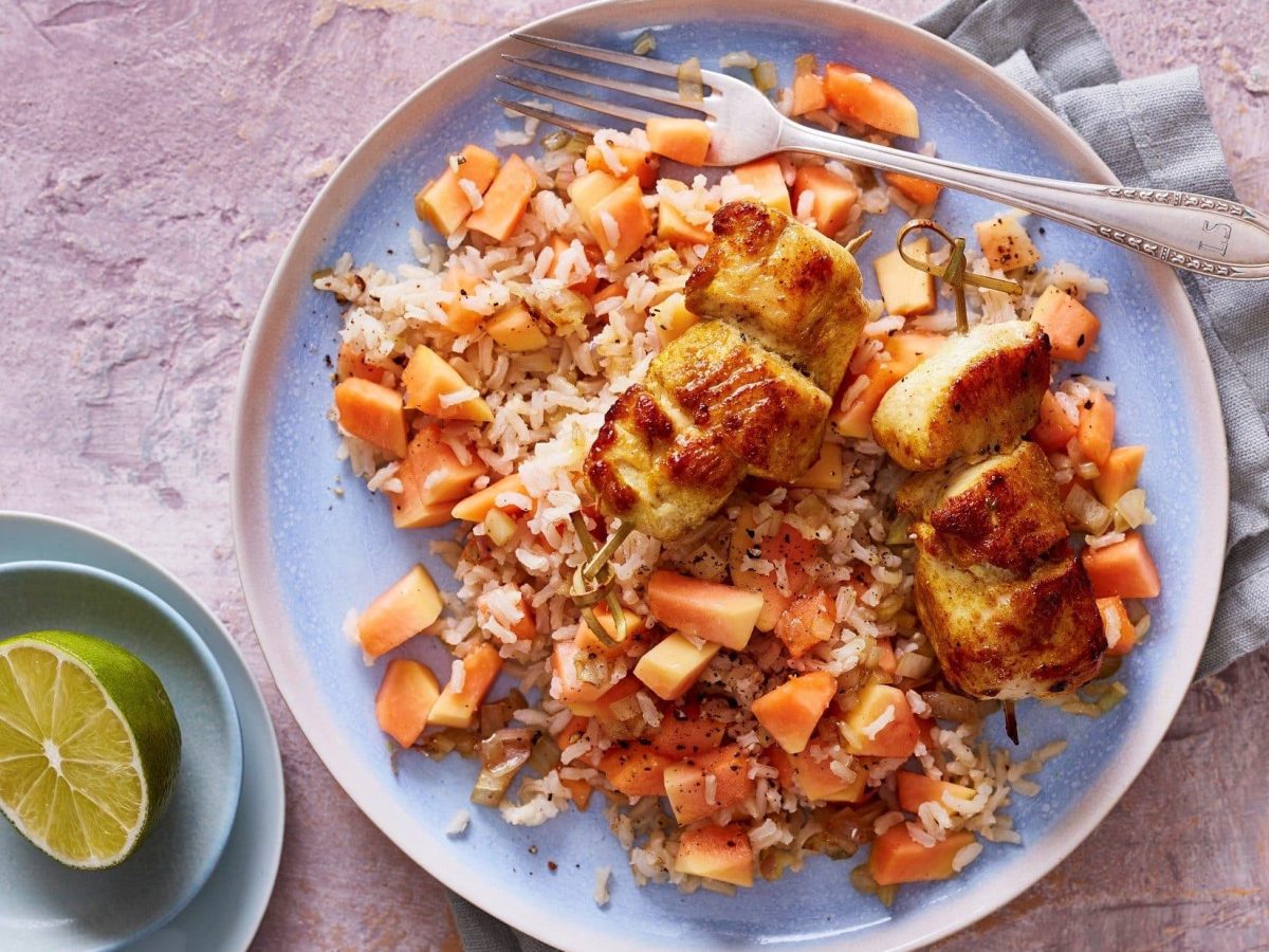 Unsere krossen Hähnchen-Spieße liegen auf fruchtigem Papaya-Salat auf einem Teller.