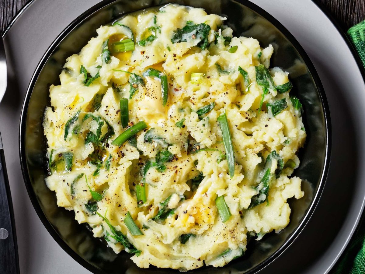 Irisches Colcannon, bestehend aus Kartoffelbrei, Grünkohl, Butter, Knoblauch und Sahne, in einer Auflaufform gebacken und auf einem schwarzen Teller serviert