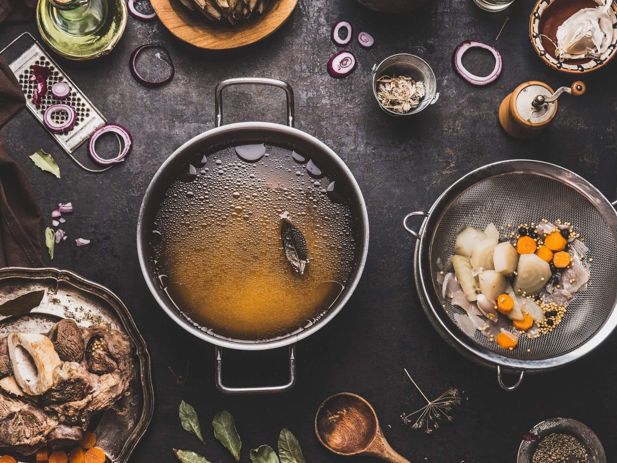 Allerhand Töpfe mit Jus, Demi-Glace, Bratensauce oder Glace sowie Küchenutensilien, die etwas mit Saucen zu tun haben auf schwarzem Tisch.