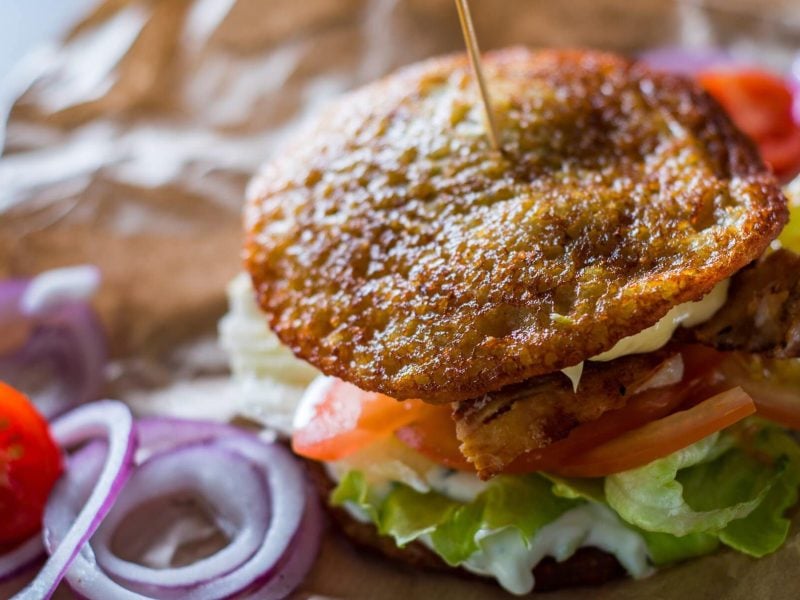 Kartoffel-Burger mit Burgerpatty, Salat und Tomaten, daneben liegen einige Zutaten.