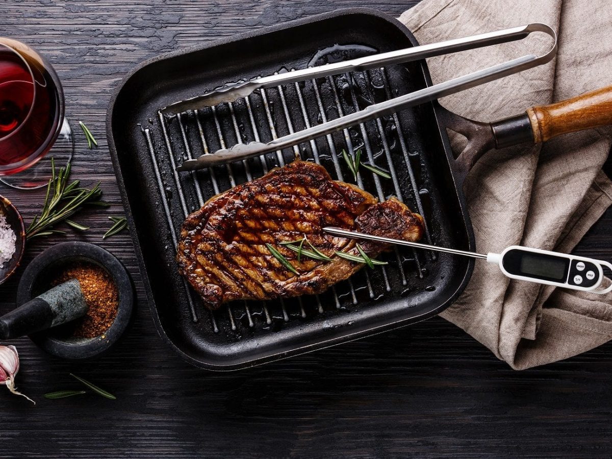 Ein Rinderfilet liegt in einer Grillpfanne, die auf dem Tisch steht. Im Rinderfilet steckt ein Thermometer.