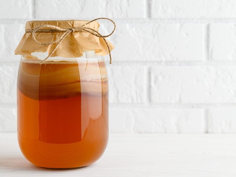 Ein Fermentationsglas mit selbst gemachtem Kombucha vor einer weißen Ziegelwand.