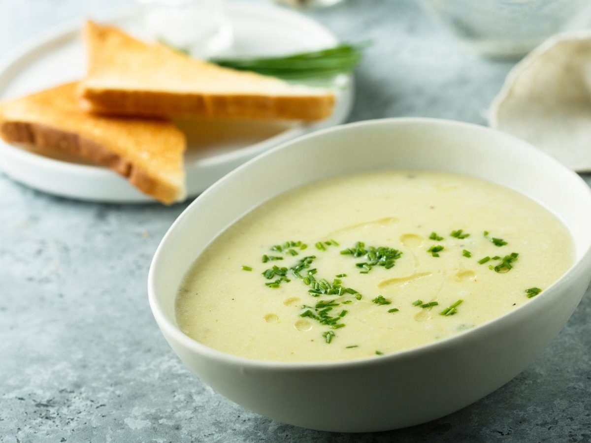 In einer weißen Schüssel ist eine meerrettich-kartoffel-suppe. Neben der Schüssel liegen zwei Toast-Hälften