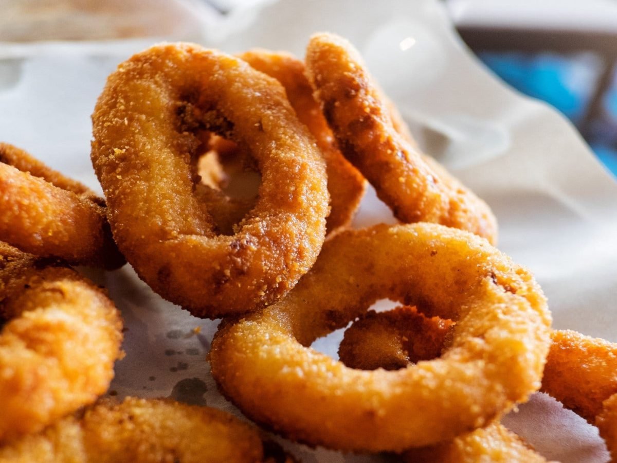 Ein paar Onion Rings in Bierteig auf einer weißen Servierplatte.