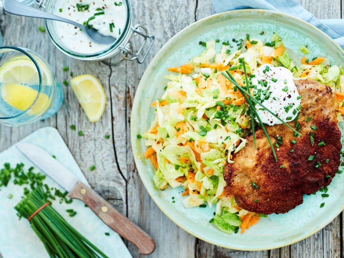 Unser paniertes Nackensteak mit Krautsalat liegt bunt angerichtet mit Schnittlauch auf einem Teller.