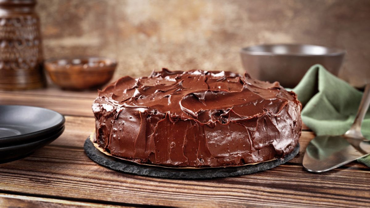 Rote-Bete-Schokokuchen mit cremiger Schokoglasur auf einer Platte auf hölzernem Untergrund