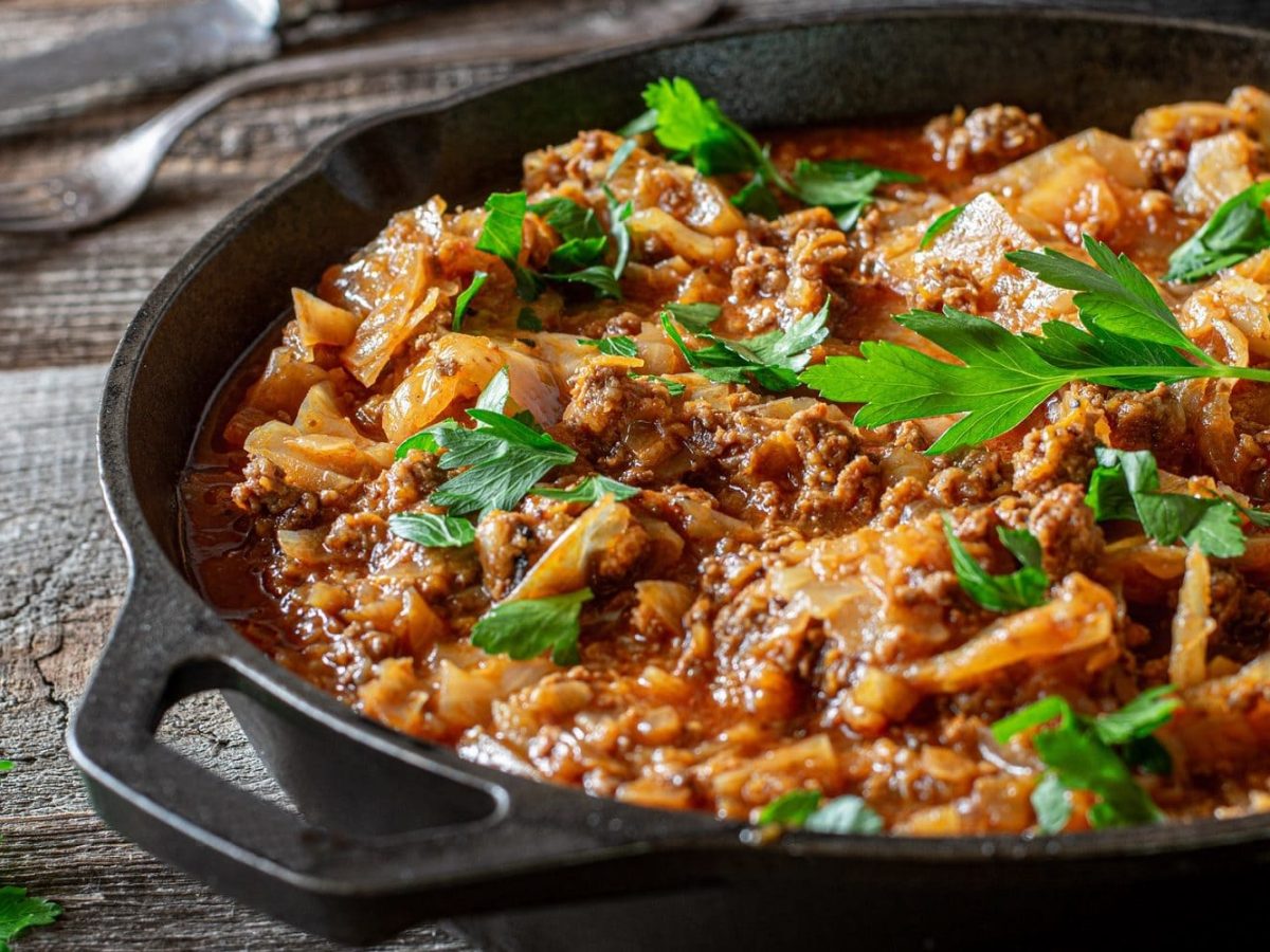 Auf einem Holztisch steht eine Weißkohl-Hackfleisch-Pfanne