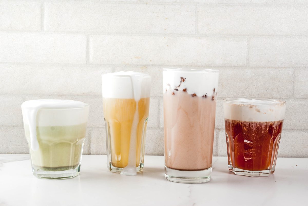 Vier Gläser mit verschiedenfarbigen Cheese-Tea-Sorten stehen auf einem weißen Tisch vor einer weißen Wand.