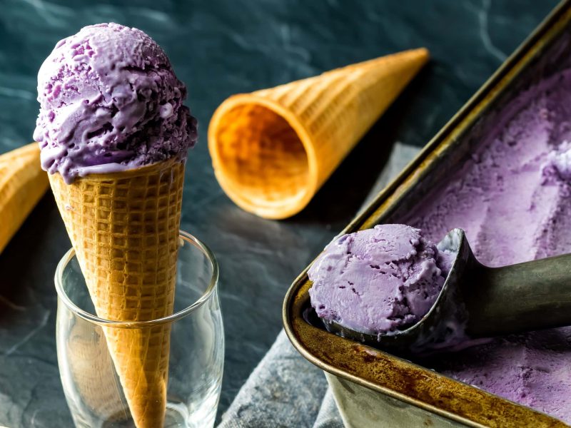 Ube-Eiscreme mit Ausstecher und Waffel auf dunkelgrünem Untergrund