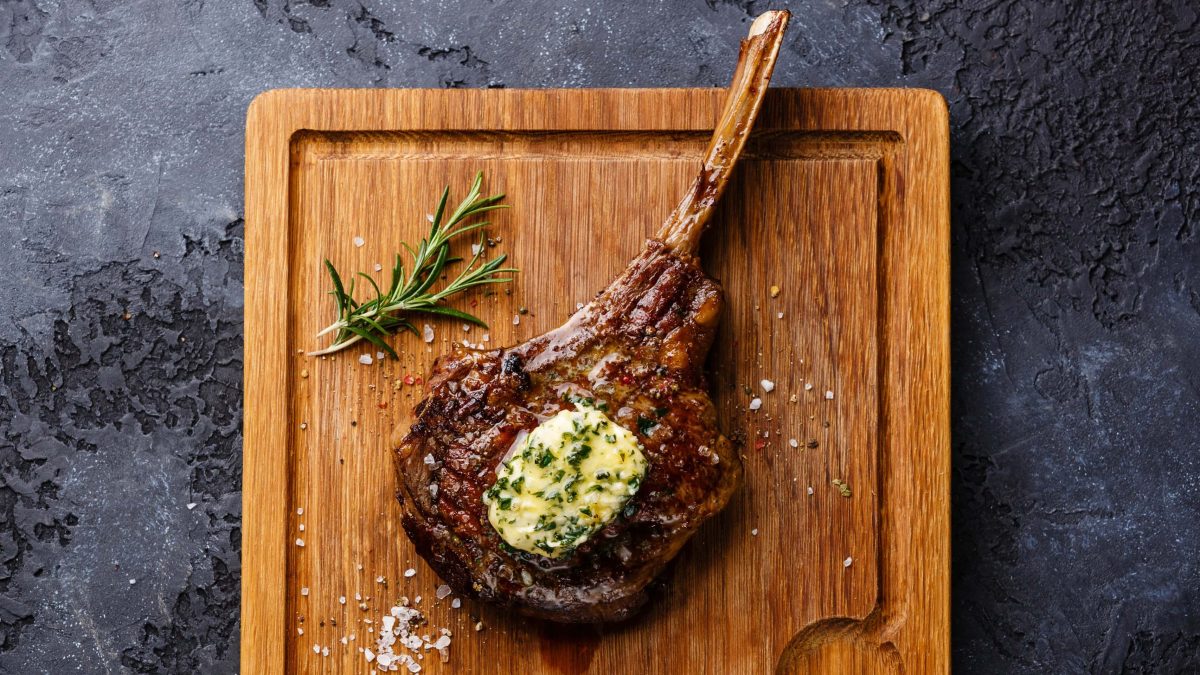 Steak von oben mit Butter auf Holzbrett und schwarzem Tisch