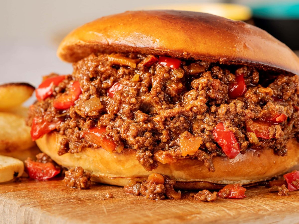 Seitliche aufnahme eiens sloppy joes mit Kartoffeln im hintergrund auf holzbrett