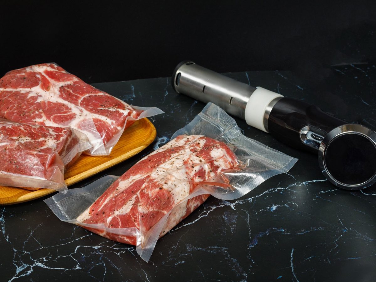 Sous-Vide Stab rechts und zwei vakuumierte Beutel mit rindfleisch links auf schwarzem Tisch