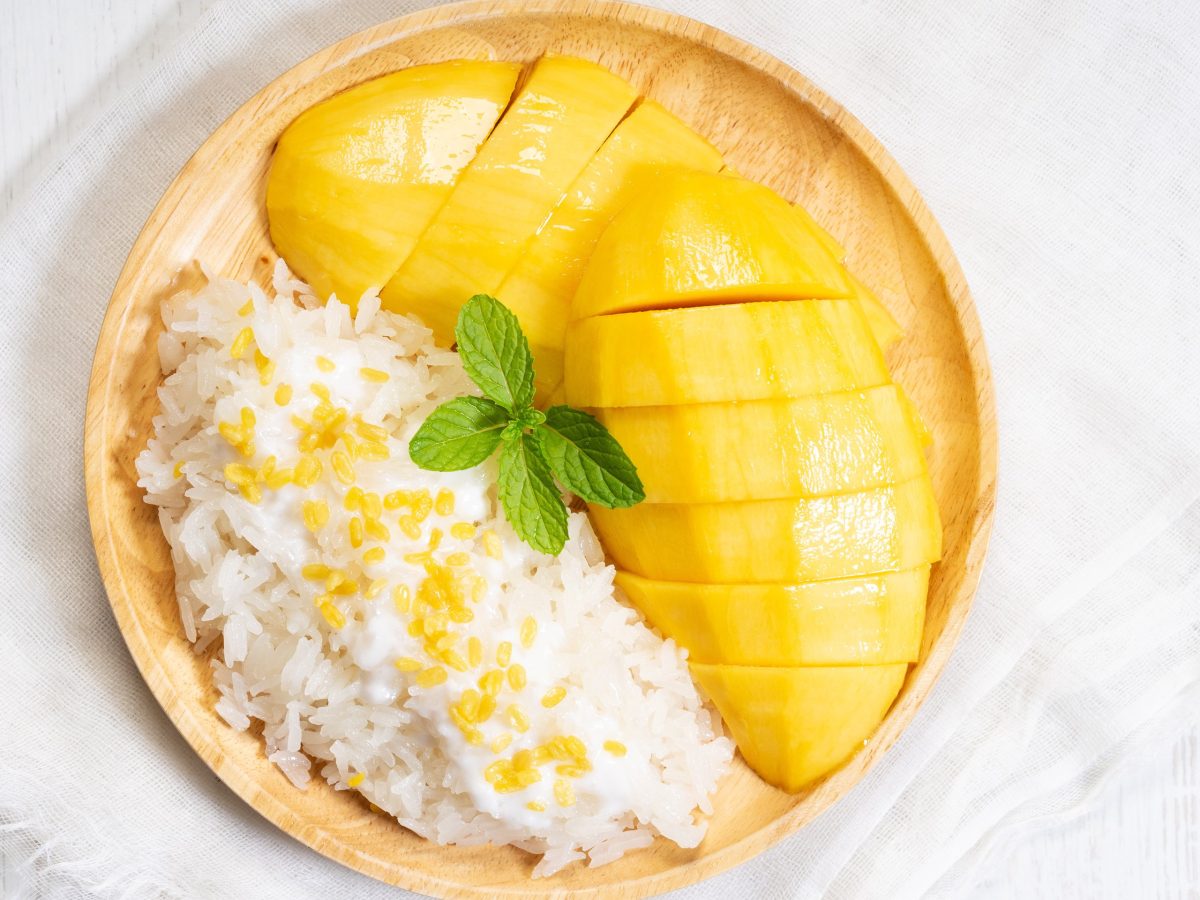 Sticky Rice mit geschnittener Mango und Kokossauce, dekoriert mit einem Minzblatt.