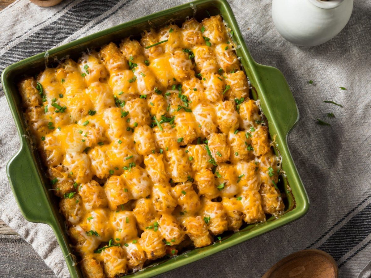 Tater Tot Hot Dish in grünr Auflaufform auf Tuch und Holztisch. Aufnahme aus der Vogelperspektive.