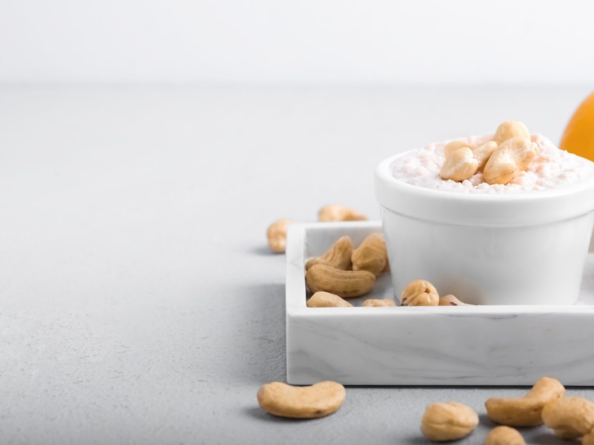 Eine Schale vegane Sour Cream mit Cashekernen auf einem Tablett, daneben liegt eine halbierte Zitrone.