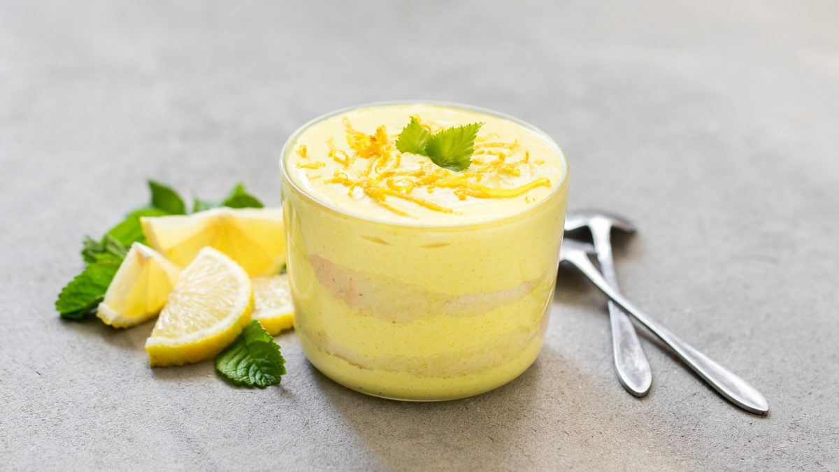 Vegane Zitronencreme mit Biscuitstückchen und frischer Minze serviert in einem durchsichtigen Glas auf steinernem Untergrund