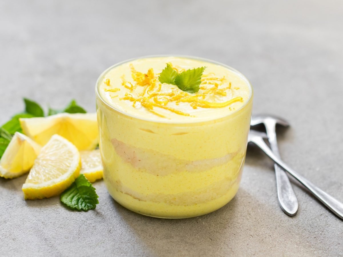 Vegane Zitronencreme mit Biscuitstückchen und frischer Minze serviert in einem durchsichtigen Glas auf steinernem Untergrund