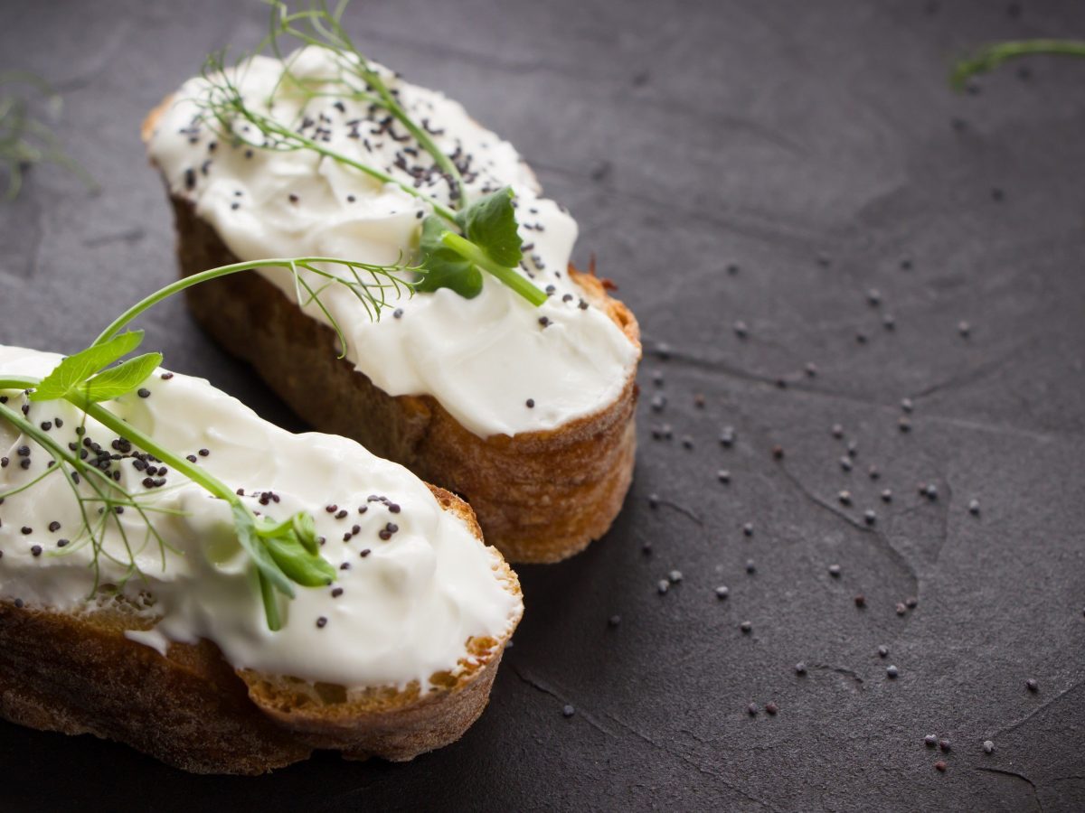 Veganer Frischkäse auf Brotscheiben, garniert mit Microgreens auf einer schwarzen Schieferplatte