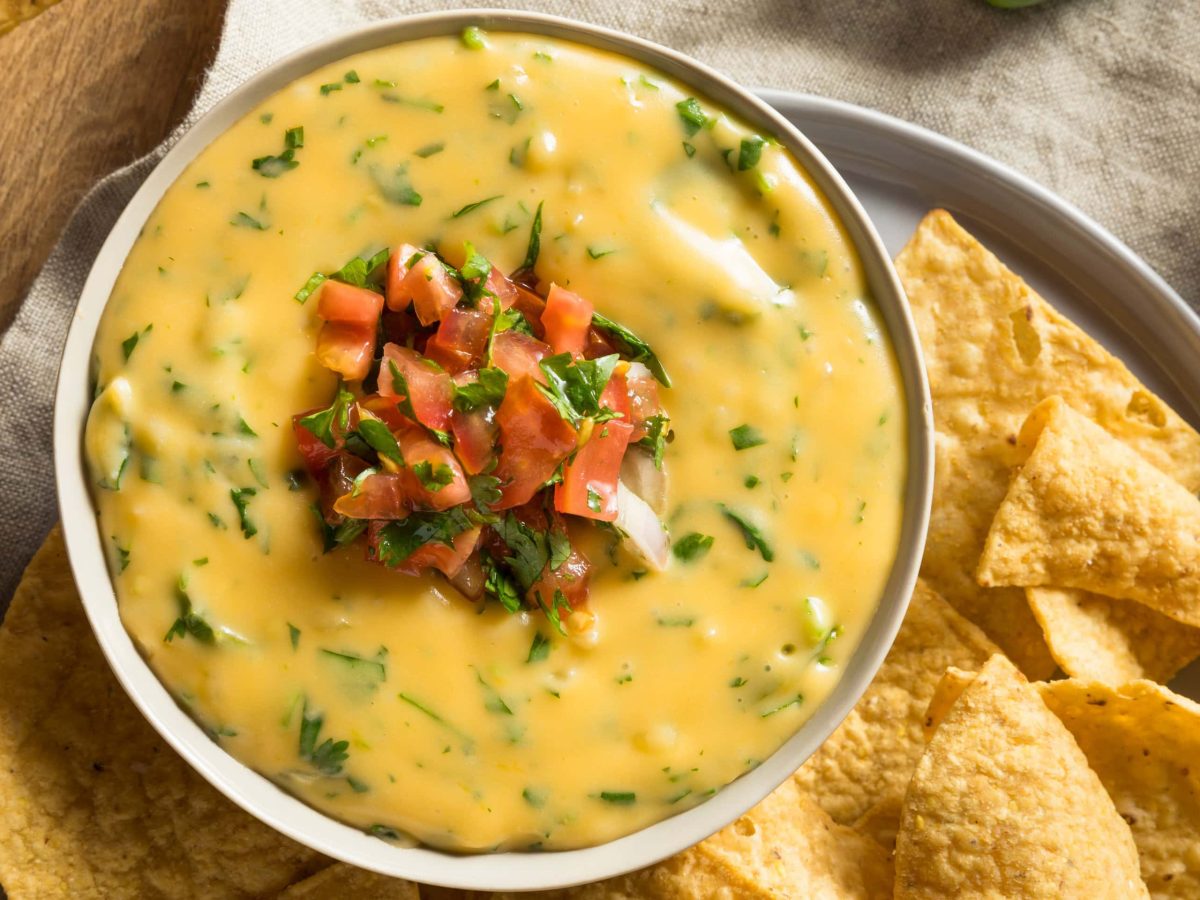 Eine Schale veganer Käsedip mit geschnittenen Tomaten und Kräutern sowie Nachos.