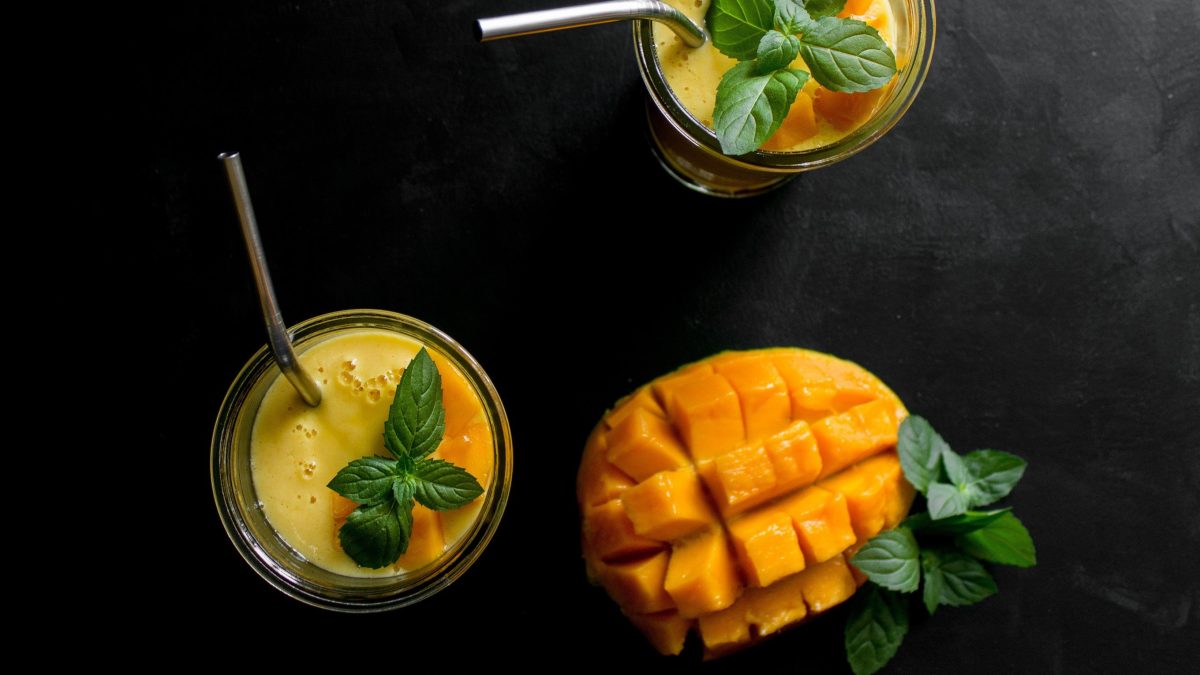 Veganer Mango-Lassi in Gläsern aus der Vogelperspektive, garniert mit frischer Minze auf Schieferplatte