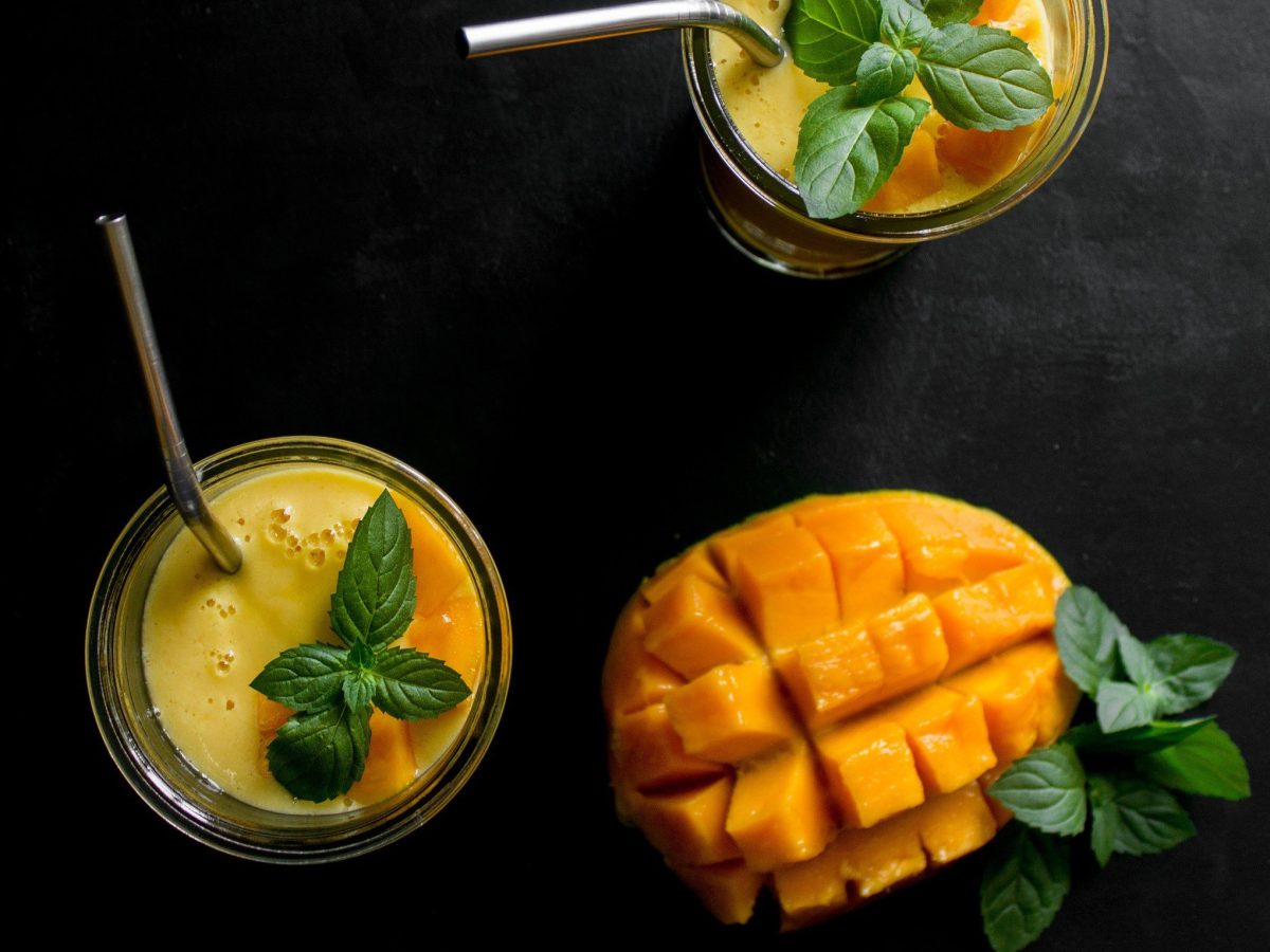 Veganer Mango-Lassi in Gläsern aus der Vogelperspektive, garniert mit frischer Minze auf Schieferplatte